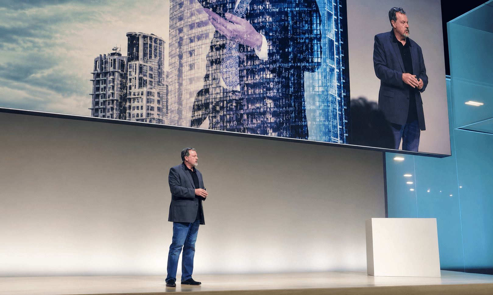 Louis Richardson speaking onstage beneath a large presentation screen